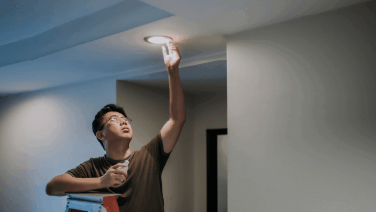 man standing on a ladder, installing an LED light bulb
