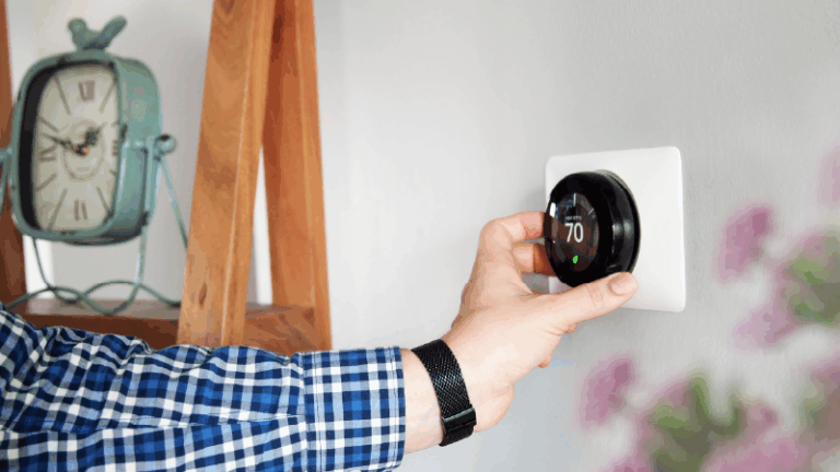 person adjusting a thermostat that happens to be by a clock